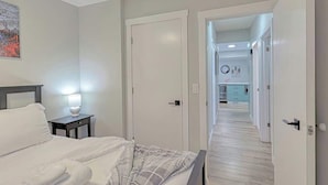 A hotel room with a bed, bedside table, and a hallway leading to a kitchen area.