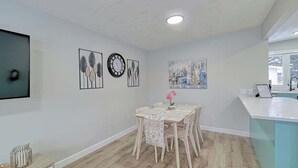 A modern kitchen with a white countertop, a dining area with a table and chairs, and artwork on the walls.