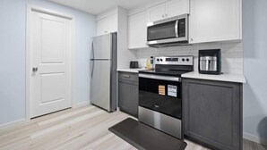 A modern kitchen with white cabinets, a stainless steel refrigerator, a microwave, an oven, and a coffee maker.