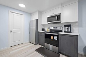Una cuina moderna amb armaris blancs, un refrigerador d'acer inoxidable, un microones, un forn i una cafetera.