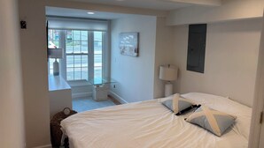 A bedroom with a bed, a window, a lamp, and a painting on the wall.