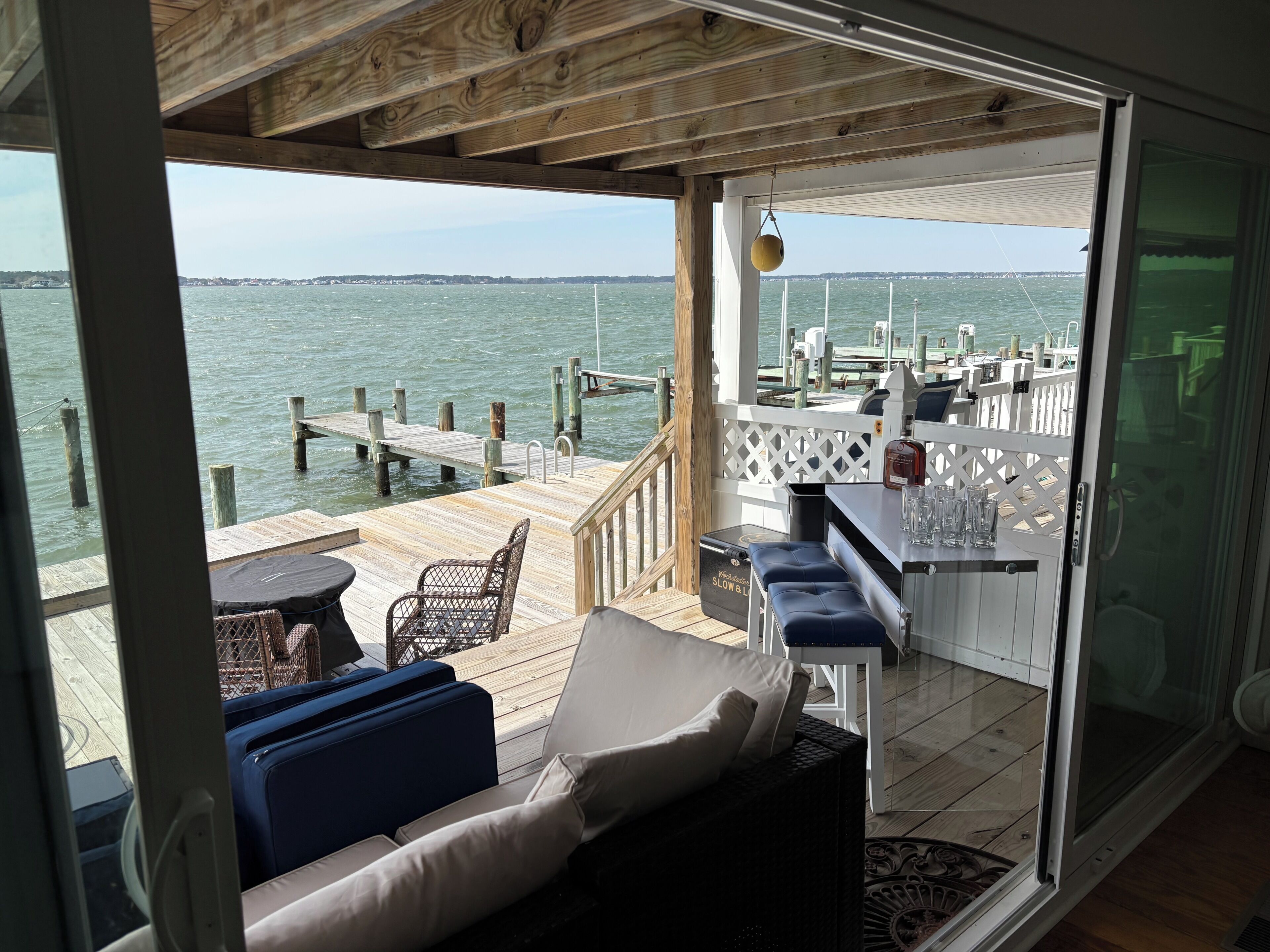 A wooden deck with a seating area, a bar, and a view of the water.