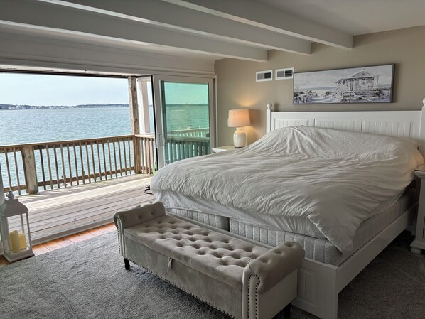 Ein Schlafzimmer mit einem großen Bett, einer Bank, einem Nachttisch mit Lampe und Blick aufs Wasser.