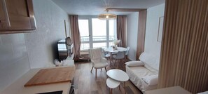 Ein kompakter Wohnbereich mit Küchenzeile, einem Essbereich mit rundem Tisch und Stühlen, einer Couch und einem großen Fenster für natürliches Licht.