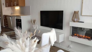 Ett modernt vardagsrum med en platt-TV, en öppen spis och ett kök i bakgrunden.
