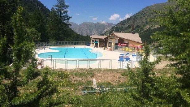 En swimmingpool med en byggnad i bakgrunden, omgiven av berg.
