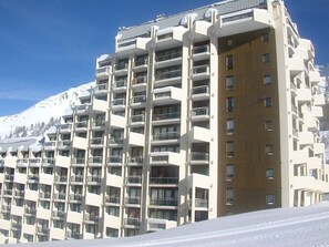 Ein mehrstöckiges Hotel mit Balkonen, einer Holzfassade und einem verschneiten Berggipanorama.