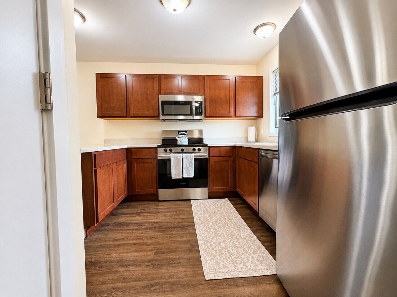 A kitchen with wooden cabinets, stainless steel appliances, and a patterned rug.