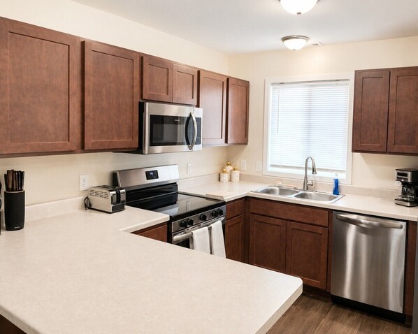 A modern kitchen with wooden cabinets, stainless steel appliances, and a window with blinds.
