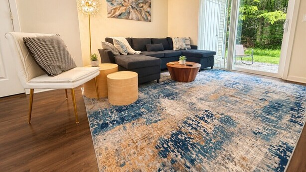 A living room with a sofa, two side tables, a chair, and a large rug. - Holiday Village Townhomes – 3883 (Traverse City)