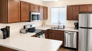 A modern kitchen with wooden cabinets, stainless steel appliances, and a white countertop. - Holiday Village Townhomes – 3883 (Traverse City)