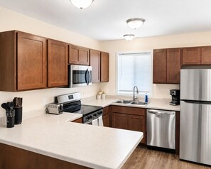 A modern kitchen with wooden cabinets, stainless steel appliances, and a white countertop.