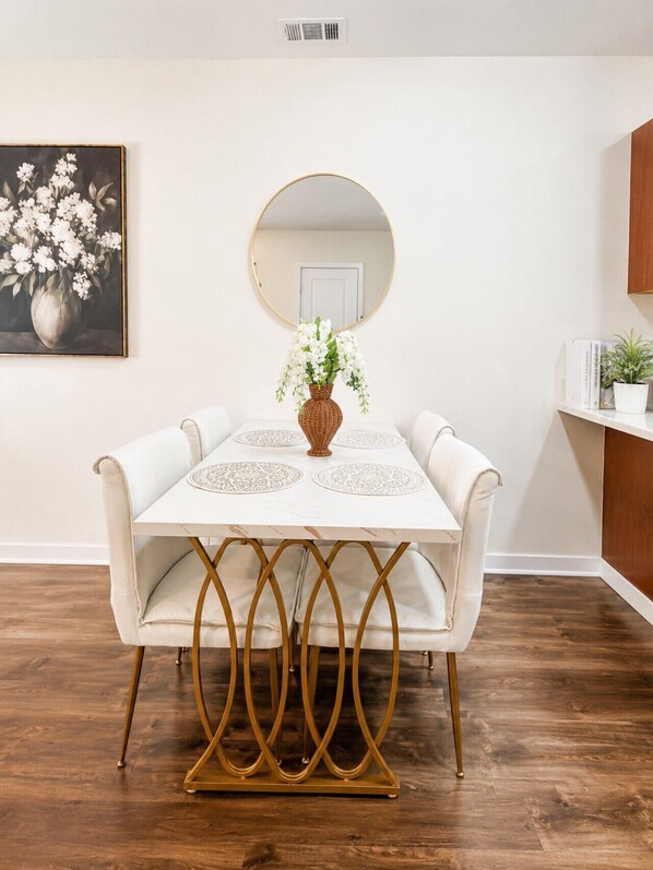 A dining table with a vase of flowers, a mirror above it, and a white wall. - Holiday Village Townhomes – 3883 (Traverse City)