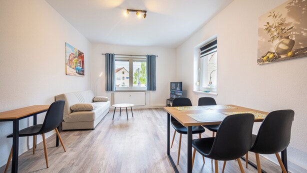 Ein modernes Wohnzimmer mit einer Couch, einem Esstisch mit Stühlen, einem Fernseher und Kunstwerken an den Wänden.