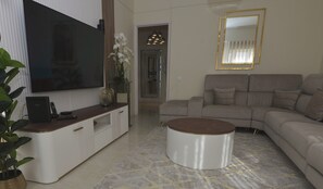 Ein modernes Wohnzimmer mit Flachbildfernseher, einer Couch, einem Couchtisch und einem Konsolentisch mit Blumen in einer Vase.