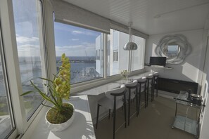 A modern kitchen with a large window, a potted plant, bar stools, a TV, and a decorative mirror. - Luxury Ocean View (Ponta Delgada)