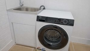 En kompakt tvätt- och torkmaskin med ett inbyggt handfat, placerad i ett litet tvättrum med vita väggar och kaklat golv.
