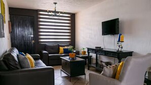 A living room with a sofa, armchair, TV, and a small table with a plant. - Casa AMAR-i-LLA - Centrally located and with A/C (Guadalajara)
