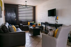 A living room with a sofa, armchair, TV, and a small table with a plant.