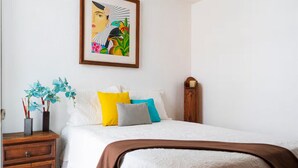 A bedroom with a bed, pillows, a nightstand, a framed artwork, and a wooden nightstand. - Casa AMAR-i-LLA - Centrally located and with A/C (Guadalajara)