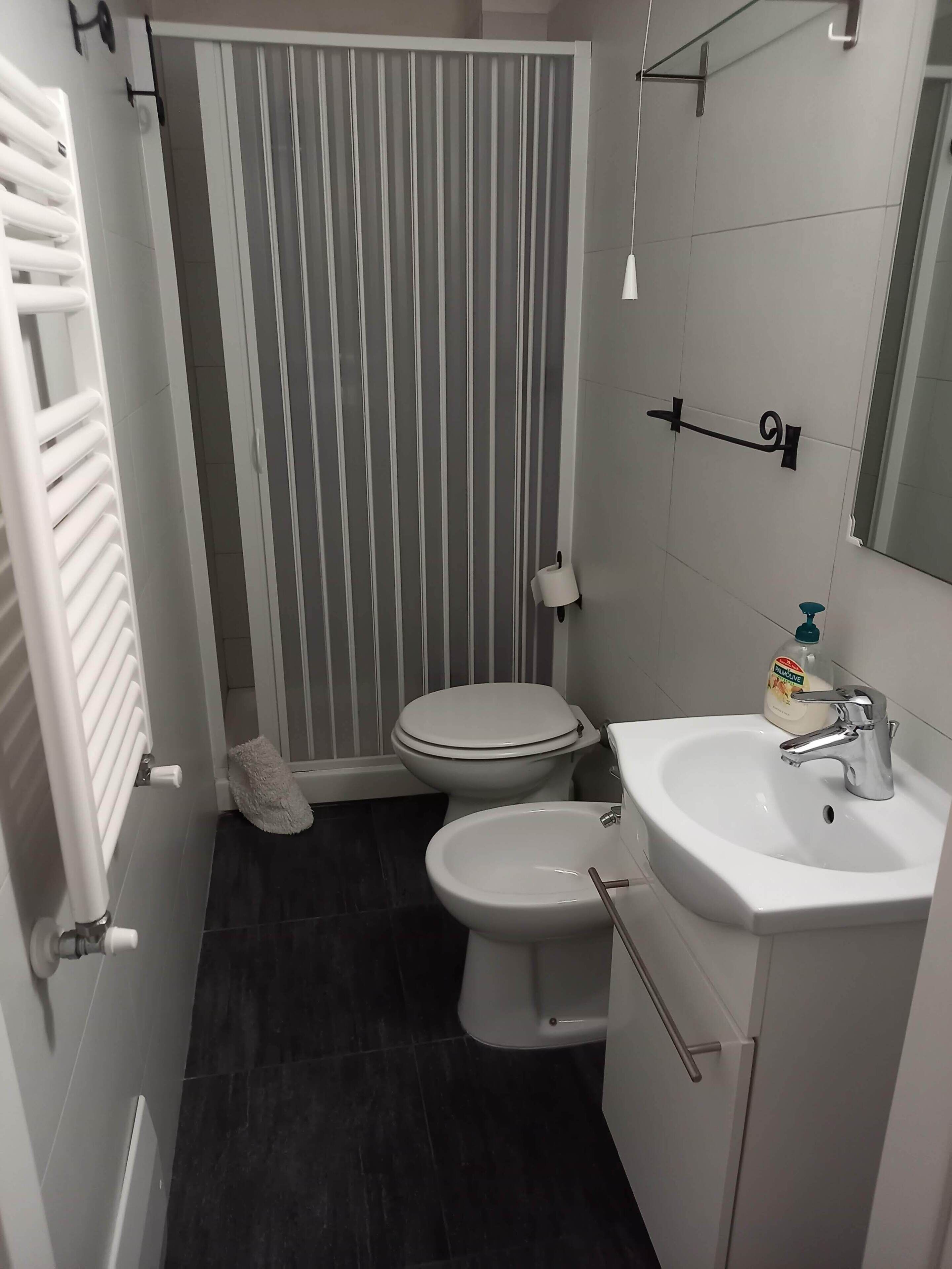 Un baño con inodoro, bidé, lavamanos blanco y un perchero para toallas.