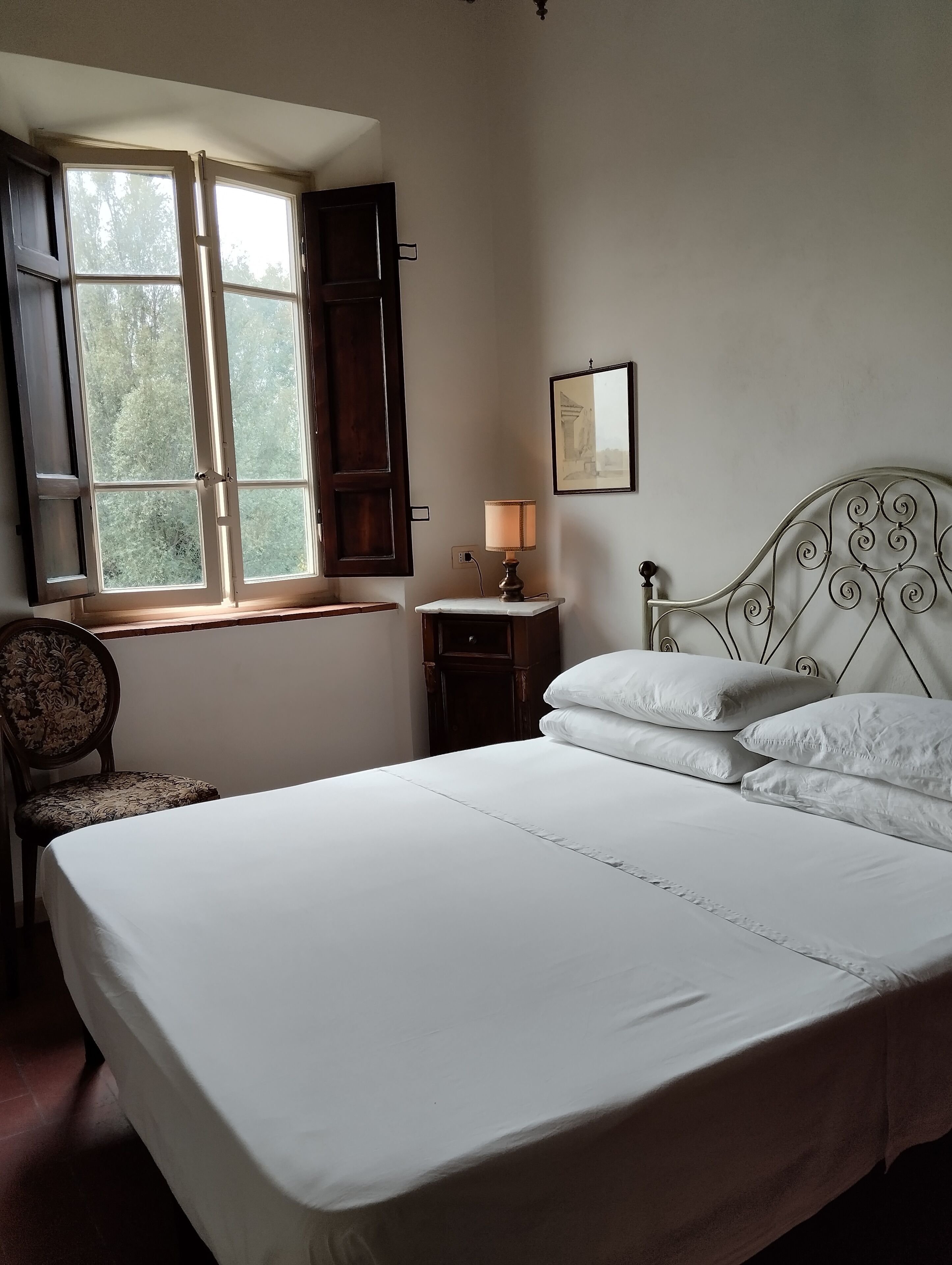 Quarto com cama, cadeira, mesa de cabeceira, luminária e janela com cortinas.