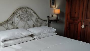 A neatly made bed with white linens, a metal headboard, a bedside table with a lamp, and a wooden wardrobe.