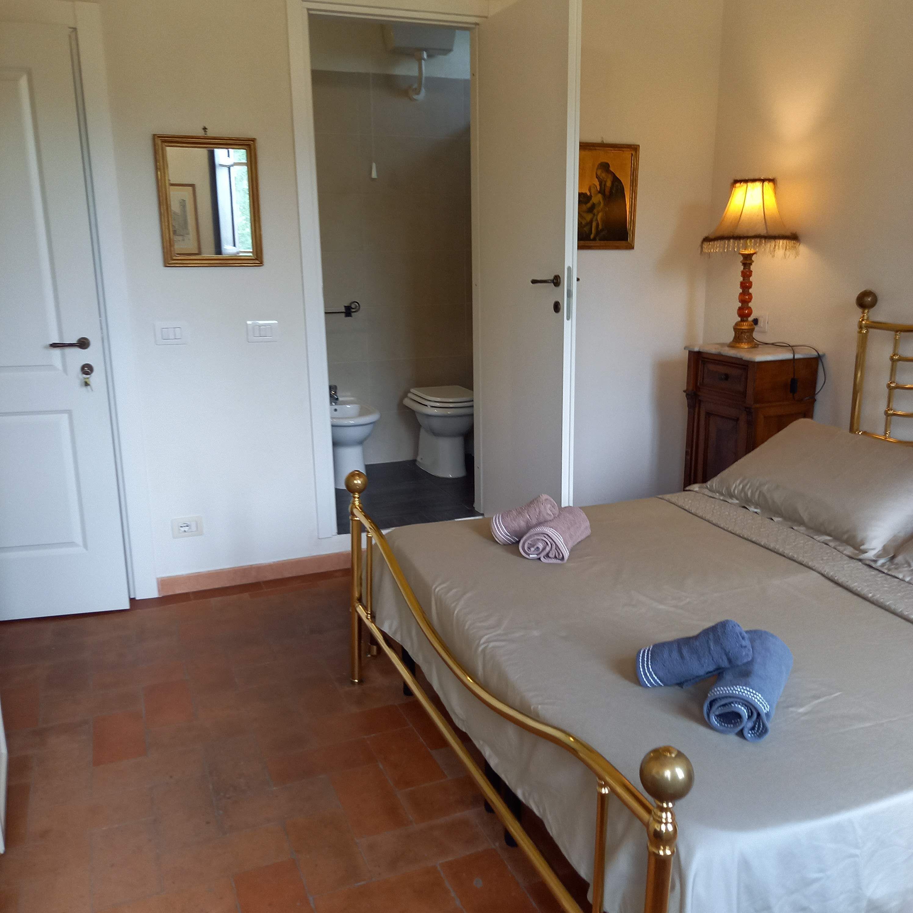 Une chambre à coucher avec un lit, une table de chevet avec une lampe, une porte donnant sur une salle de bain et un petit tableau accroché au mur.