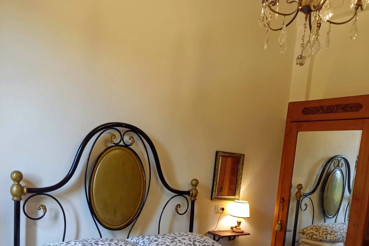 Una cama con una colcha estampada, una lámpara de noche, un espejo y una araña.