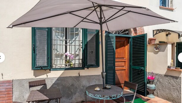 A patio with a table and chairs, a large umbrella, and a window with shutters. - CHARMING LUCCA (Lucca)