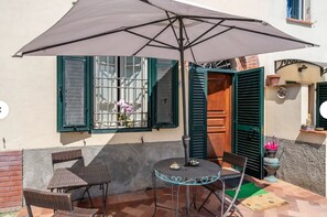 Un patio con una mesa, sillas, una sombrilla grande y una ventana con contraventanas.