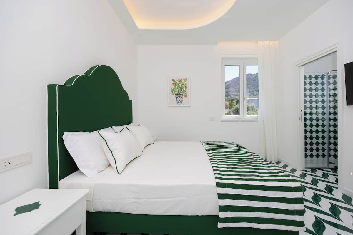 A bedroom with a bed, a bedside table, a window with a view, and a shower area.