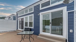 A modern building with large windows, a covered patio with a table, and a garage door. - De La Float - Floating House on Lake Cumberland (Russell Springs)