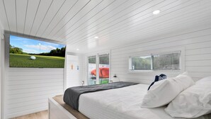 Una camera da letto con un letto, una televisione a parete, una finestra e una porta.