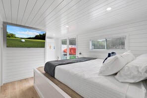 Une chambre à coucher avec un lit, un téléviseur fixé au mur, une fenêtre et une porte.
