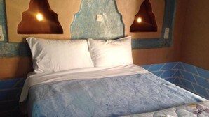 A bed with a blue quilt, white pillows, and a floral-patterned blanket. - Kasbah Ifri (Souk Lakhmis Dades)