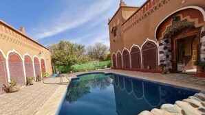 A swimming pool with stone tiles and a brick building with arched windows. - Kasbah Ifri (Souk Lakhmis Dades)