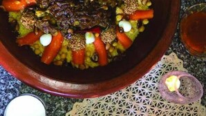 A large, round, dark-colored serving dish filled with a colorful meal, possibly a stew or casserole, with visible ingredients like carrots and chickpeas. - Kasbah Ifri (Souk Lakhmis Dades)