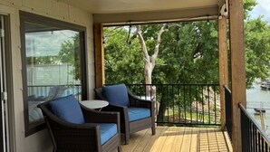 Een overdekt terras met twee rieten stoelen en een kleine tafel, met uitzicht op water en bomen.