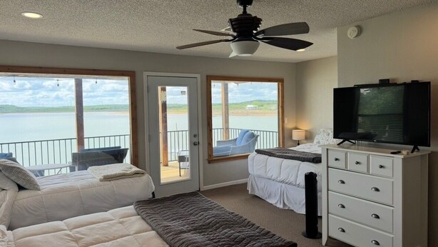 Een slaapkamer met een bed, een televisie, een dressoir en een balkon met uitzicht op het water.