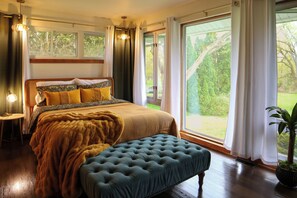 Une chambre avec un grand lit, un banc, une plante en pot et une vue sur la verdure à l’extérieur.