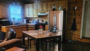 Une cuisine chaleureuse avec des meubles en bois, un réfrigérateur en acier inoxydable, une table à manger avec des chaises et un luminaire suspendu.