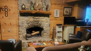 Un salon chaleureux avec une cheminée en pierre, des murs en bois, un canapé en cuir et un téléviseur.