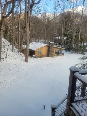 A wooden cabin with a stone chimney, surrounded by snow-covered trees and a clear sky. - The Extra House Extra Cozy Extra Cute (Clayton)