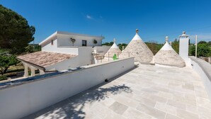 A rooftop terrace with a white building, stone conical structures, and a clear blue sky. - Villa 'Trulli San Domenico' with Private Pool, Wi-Fi and Air Conditioning (Martina Franca)