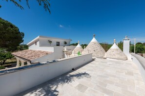 Una terraza en la azotea con un edificio blanco, estructuras de piedra cónicas y un cielo azul despejado.
