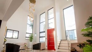 A spacious room with a high ceiling, large windows, a staircase, and a red door. - Spacious Luxury Villa - Pool, Jacuzzi & View. (Camu)