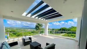 A covered outdoor seating area with sofas and a table, overlooking a scenic landscape. - Spacious Luxury Villa - Pool, Jacuzzi & View. (Camu)