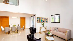 A spacious living area with a high ceiling, a sofa, a coffee table, and a dining table with chairs. - Spacious Luxury Villa - Pool, Jacuzzi & View. (Camu)