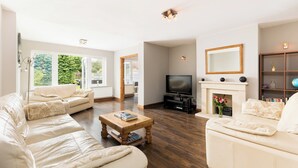 A living room with a sofa, a coffee table, a TV, a fireplace, and a bookshelf. - Central Bourton Gem|5 Bedrooms|Garden|Parking - Pass the Keys (Bourton-on-the-Water)